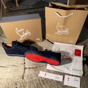 Mörkblå Cristian Louboutin  - Snygga mörkblå sneakers från Christian Louboutin med den ikoniska röda sulan. Skorna har snörning och är tillverkade i mocka, vilket ger en lyxig känsla. Perfekta för den som vill ha en stilren och exklusiv look.