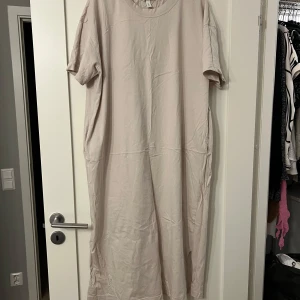 Beige klänning från H&M - Säljer en stilren beige T-shirt klänning från H&M. Den har en enkel design med korta ärmar och en rund halsringning. Perfekt för en avslappnad look.