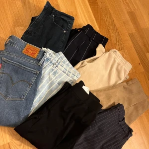 Samling av olika byxor - En samling av olika byxor inklusive Levis jeans, randiga kostymbyxor och beige chinos. Perfekt för att variera garderoben med olika stilar och material. Alla är i storlek XS-S