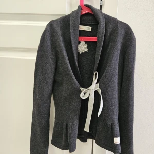 Mörkgrå kofta från Odd Molly stl 0 - Säljer en elegant mörkgrå kofta från Odd Molly med knytband framtill och en broderad detalj på ryggen. Koftan har långa ärmar och en fin volangdetalj vid nederkanten. Perfekt för kyliga dagar! Jättefin skick 