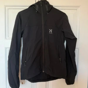 Svart vindjacka från Haglöfs - Säljer en svart vindjacka från Haglöfs i storlek S för dam. Jackan har en dragkedja framtill och två praktiska fickor med dragkedjor. Perfekt för blåsiga dagar med sin lätta och funktionella design.