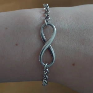 Silverfärgat armband med oändlighetssymbol - Snyggt silverfärgat armband med en oändlighetssymbol i mitten. Armbandet har en kedja med små länkar och ett enkelt lås.♾️