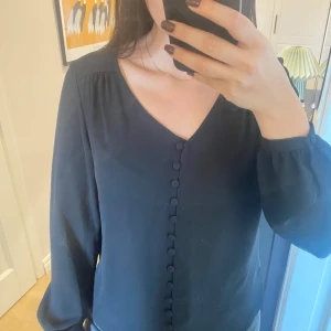 Svart blus från VILA - Elegant svart blus från VILA med v-ringning och knappar framtill. Blusen har långa ärmar och är i ett tunnare material. Aldrig använd.