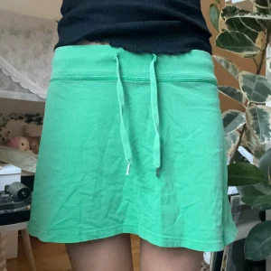 Grön kjol från H&M - Säljer en grön kjol från H&M med knytband i midjan och en liten blommig detalj längst ner! 🌺Kjolen har en ficka bak och är perfekt för sommaren!