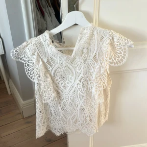 Vit spetsblus från Zara - Säljer en vacker vit spetsblus från Zara med intrikata mönster och korta ärmar. Perfekt för en elegant look med sin delikata spetsdesign och luftiga passform. Blusen har en rund hals och är tillverkad i ett lätt material💞💞
