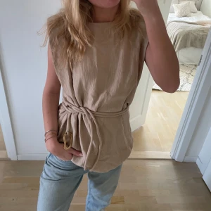 Beige topp med knytband - Snygg beige topp med knytband i midjan. Perfekt för en stilren look. Passar bra till jeans eller kjol.