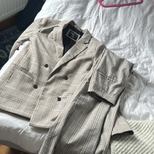 Rutig kavaj och byxor från FB Sister - Snyggt set med rutig kavaj och matchande byxor från FB Sister( New yorker ) . Kavajen har dubbelknäppning och klassisk krage. Perfekt för en stilren look.Byxorna är boot cut ( tajta vid låren , hängiga vid benen ) 400 kr för båda , 250 för kavajen och 150 för byxorna OBS No free shipping , går ej att ta bort 