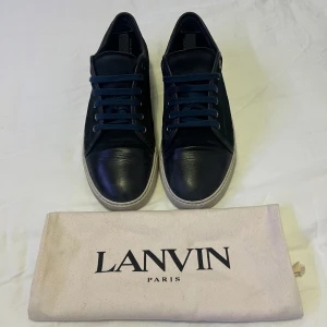 Marinblåa Lanvin - Säljer ett par marinblpa sneakers från Lanvin med vita sulor och mörkblå snörning. Skorna har en klassisk rund tå och platt sula. Perfekta för dig som gillar stilrena och exklusiva sneakers. Medföljer originalpåse från Lanvin. Priset är inte hugget i sten