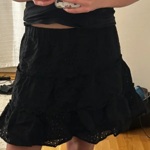 Svart kjol med volang från FB Sister - Supersöt svart kjol från FB Sister i storlek XS. Kjolen har volanger och broderade hål som ger en extra detalj. Perfekt för dig som gillar en feminin och trendig stil. Resår i midjan för skön passform. Säljer pga inte min stil längre❤️🫶🏻