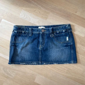 Jeans minikjol - Säljer en klassisk blå jeans minikjol. Kjolen har slitna detaljer och rå kant nertill för en cool look. Perfekt till sommaren! Midjemått 39cm