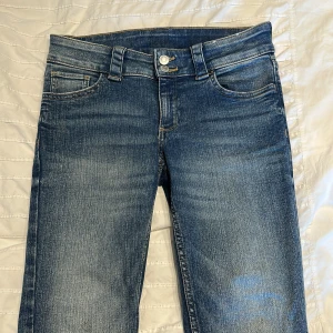 Blåa bootcut jeans från H&M. - Säljer ett par klassiska blå jeansbyxor från H&M med bootcut form. Byxorna har fem fickor, knapp och dragkedja framtill samt snygga slitningar för en avslappnad look.