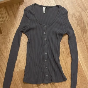 Mörkgrå ribbad kofta  - Säljer en mörkgrå ribbad kofta med långa ärmar och knappar framtill. Tröjan har en tight passform och är perfekt att styla till olika outfits. Använd fåtal gånger. 