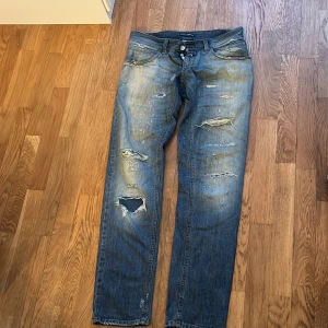 Dolce & Gabbana slitna blå jeans - Säljer ett par blå jeans från Dolce & Gabbana med slitna detaljer och hål på benen. Jeansen har klassisk femficksdesign, knappar och dragkedja framtill samt patch med logga på bakfickan. Tillverkade i bomull.