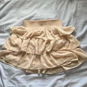 Beige volangkjol med resårmidja - Supersöt beige kortkjol med flera lager volanger och bred smockad resår i midjan. Kjolen har en luftig och flowy känsla, perfekt för varma dagar. Passar dig som gillar romantisk och feminin stil. Kan också användas som en söt topp! Kom privat för mått eller fler frågor, pris kan diskuteras💕