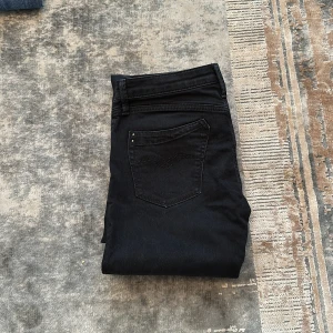 Svarta jeansbyxor från Replay - Svarta jeansbyxor från Replay med klassisk femficksdesign och raka ben. Byxorna har silverfärgade knappar och dragkedja, samt diskreta sömmar på bakfickorna. Perfekta för en stilren och enkel look.