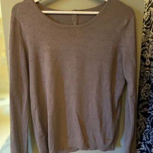 Ljuslila stickad tröja med prickar från Mango - Säljer en ljuslila stickad tröja från Mango med diskreta prickar i materialet. Tröjan har rund halsringning, långa ärmar och knappar i nacken. Perfekt för lager-på-lager och enkel att matcha.