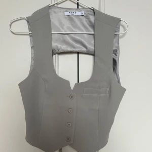 Grå väst från NA-KD - Snygg grå väst från NA-KD collektion med Lojsan Wallin.  Västen har en figurnära passform och kan justeras i ryggen. Aldrig använd tyvärr pga för stor storlek. Men den är SÅ fin!!