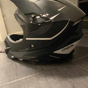 Svart och vit hjälm från O'Neal - Säljer en svart och vit O'Neal-hjälm med sportig design och tydliga logotyper på sidorna och ovansidan. Hjälmen har visir, ventilation och justerbart hakspänne. Passar perfekt för intensiva aktiviteter.