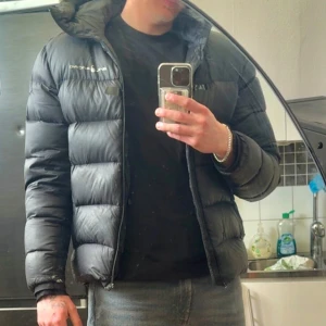 Svart dunjacka från Sail Racing - Säljer en klassisk Sail Racing dunjacka i svart, storlek Large.  Varm och funktionell med sportig look – passar perfekt för kalla dagar både i stan och ute i naturen.     [NOTERING] mycket sliten och fler defekter, syns i bilderna! Kedjan är dålig på den   • Storlek: Large • Passform: Normal, något längre, • Färg: Svart • Material: Dunfylld, vattenavvisande • Broderad Sail Racing-logga på bröst  • Justerbar midja • Innerficka, luva