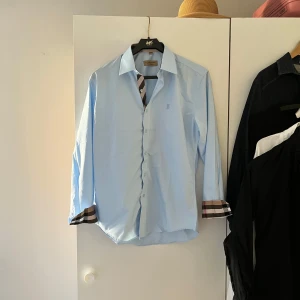Ljusblå skjorta från Burberry med rutiga detaljer - Hej! Säljer nu denna otroligt feta burberry skjortan, den är i väldigt bra skick typ 9/10 inga defekter alls, storlek M passar 175-185 cm, bara att höra av sig vid funderingar och pris är diskuterbart