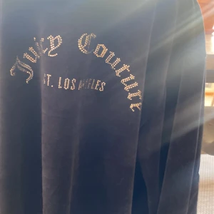 Mörkblå velourjacka från Juicy Couture - Säljer en mörkblå velourjacka från Juicy Couture med glittrande stenar på ryggen och på  loggan på framsidan. Jackan har huva, dragkedja och fickor framtill. Perfekt för en avslappnad och trendig look.