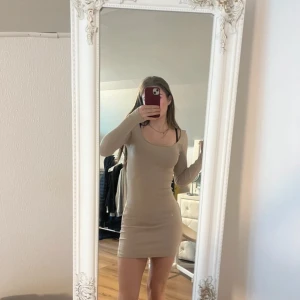 Beige långärmad tight klänning - Säljer en beige, långärmad och tight klänning med rundad halsringning. Klänningen är kort och har en enkel, stilren design som passar perfekt för dig som gillar minimalistiskt mode.