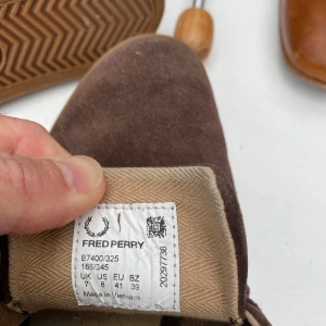 Bruna mockasneakers från Fred Perry - Säljer ett par bruna sneakers från Fred Perry i mocka med snörning och gummisula. Skorna har en låg profil och diskret broderad logga på sidan. Perfekta för dig som gillar klassisk och stilren design.