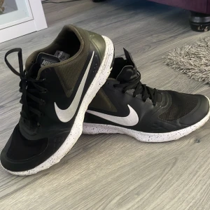 Svarta Nike sneakers med vit sula - Säljer ett par svarta Nike sneakers med vit, stänkmönstrad sula och stora vita swoosh-loggor på sidorna. Skorna har snörning och är perfekta för träning eller vardagsstil.