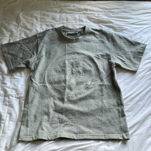 Grå t-shirt från Emma Israelsson - Snygg grå t-shirt från Emma Israelsson med ett stort präglat diamantmönster på bröstet. Klassisk passform med rund hals och korta ärmar.