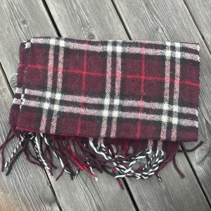 Vinröd burberry halsduk - Burberry halsduk i sådär skick den är lite noprig och tvättad någon gång men ändå relativt mjuk den har en reva i kanten och ett litet hål