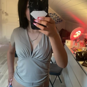 Beige omlottopp med djup v-ringning - Säljer en beige omlottopp med djup v-ringning och korta ärmar. Toppen har en snygg drapering framtill och är i ett mjukt, stretchigt material. Perfekt för dig som vill ha en stilren men ändå trendig look. Har bara använt 2-3 gånger!