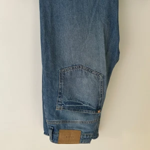 Blå 90's straight jeans från &Denim - Säljer ett par klassiska blå jeans från &Denim i modellen 90's straight med ultra hög midja. Jeansen har raka ben, fem fickor och snygga kopparfärgade nitar. Perfekta för en avslappnad och tidlös look.