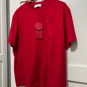 Röd t-shirt från Magda Butrym strl S- ny med lappar! - Säljer en röd t-shirt från Magda Butrym med broderad ros på bröstet och  logga bak på ryggen nacken. Snygg oversize modell som utan problem passar strl xs till M.Strl Small ny med lappar. Frakar snabbt!