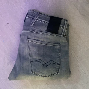 Gråa jeans från replay - Säljer ett par grå jeansbyxor från Replay Anbass med klassisk femficksdesign och svart läderpatch bak i midjan. Snygg kontrastsöm på bakfickan och raka ben. Perfekta för dig som gillar stilrena och tidlösa jeans.