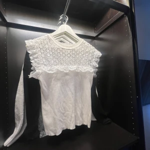 Vit blus med spetsdetaljer - Säljer en söt vit blus med vackra spetsdetaljer över axlar och bröst. Blusen har korta ärmar och en rund halsringning. Perfekt för dig som gillar romantisk och feminin stil.