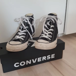Svarta Converse Chuck Taylor All Star High i storlek 36 - Klassiska svarta Converse Chuck Taylor All Star high-top sneakers med vit sula och vita snören. Skorna har rund tå, platt sula och tydliga vita sömmar. Skorna är som nya och har inga skador på sig. De är i storlek 36. Skickas inte utan måste hämtas.