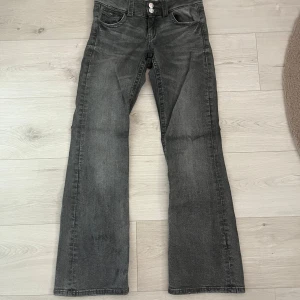 Grå bootcut jeans från Gina Tricot - Säljer ett par grå jeansbyxor från Gina Tricot med två knappar i midjan och klassiska fem fickor. Byxorna har en rak och något utsvängd passform som ger en cool vintagekänsla.