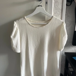 Fest tröja - Säljer en vit topp med korta ärmar och rund halsringning. Tyget har en strukturerad, lätt ribbad känsla och toppen har en enkel🥰, stilren design. Perfekt att matcha med jeans eller kjol. Perfekt fest eller sommar tröja🔥