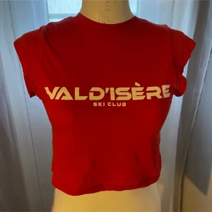Söt röd t-shirt med Val d'Isère-tryck - Snygg röd t-shirt med Val d'Isère Ski Club-tryck i vitt. T-shirten har en rund halsringning och korta ärmar. Perfekt för en avslappnad stil.