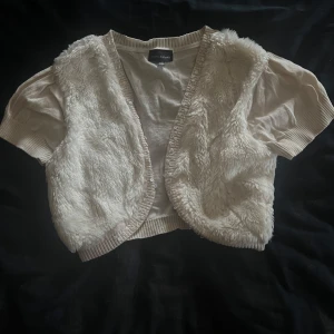 Vit pälsväst från KappAhl - Säljer en söt vit pälsväst från KappAhl med korta ärmar. Västen har ett fluffigt pälsmaterial framtill och stickade detaljer längs kanterna. Säljs för 40kr+frakt 
