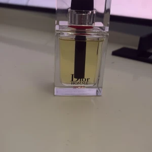 Dior Homme Sport Eau de Toilette - Fräsch och energisk herrparfym från Dior, Homme Sport. Kommer i en stilren, transparent glasflaska med svart och röd detalj på sprayhuvudet. Doften är citrusfräsch med maskulina inslag, perfekt för dig som gillar sportiga och eleganta parfymer.