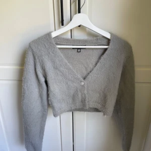 Grå croppad kofta från Missguided - Supermjuk och fluffig grå kofta från Missguided. Modellen är croppad med v-ringning och långa ärmar. Perfekt att slänga över en topp för en chill och trendig look.