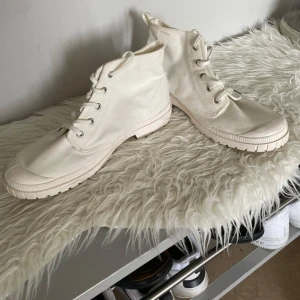 Vita Palladium boots i canvas - Säljer ett par vita boots från Palladium i canvas med snörning och rund tå. Skorna har en kraftig, mönstrad sula och klassisk logotyp på sidan. Perfekta för dig som gillar stilrena och bekväma skor med streetkänsla.