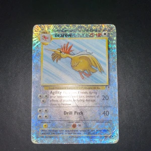 Fearow holografiskt Pokémonkort 42/110 - Säljer ett holografiskt Fearow Pokémonkort med skimrande bakgrund. Kortet har en bild på Fearow, en fågelliknande Pokémon, och innehåller attacker som Agility och Drill Peck. Baksidan har den klassiska blå Pokémon-designen med en Pokéboll i mitten.                     - Skriv vid intresse 