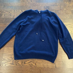 Mörkblå hoodie i kashmir från Garde Grisch - Mysig mörkblå hoodie från Garde Grisch i kashmir. Tröjan har huva, snörning och långa ärmar. Perfekt för dig som gillar en stilren och enkel look.