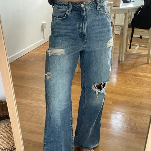 Blå wide jeans från New Look Bella - Säljer ett par blåa high waist jeans från New Look Bella med breda ben och slitna detaljer på låren och knäet. Jeansen har råa kanter nertill och klassisk femficksmodell. Perfekta för en avslappnad och trendig look.