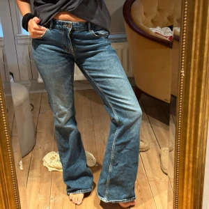 Blå bootcut jeans lågmidjade - Säljer ett par klassiska blå jeans med bootcut passform och låg midja. Jeansen har fem fickor, dragkedja och knapp framtill. Materialet är robust denim som ger en snygg vintagekänsla. Perfekta för dig som gillar en avslappnad men trendig look. Storlek 40 men sitter kanske bäst på S-M