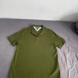 Olivgrön pikétröja Tommy Hilfiger L - Snygg olivgrön pikétröja från Tommy Hilfiger i storlek L. Klassisk krage, korta ärmar och liten logga på bröstet. Slim fit-modell i mjuk bomull med skön känsla. Perfekt för en clean och stilren look.