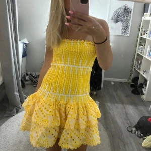 Gul och vit kort sommarklänning - Superfin axelbandslös kort klänning i gult och vitt med smockad överdel och volangig kjol. Sitter tajt upptill och har en luftig kjol som ger en härlig sommarkänsla. Kan tänka sänka priset vid snabbare affär 
