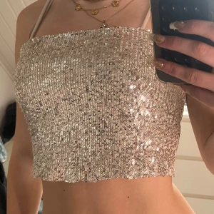 Glittrig silver tubtopp från Lindex - Supersnygg tubtopp från Lindex i silver med massor av paljetter som glittrar i ljuset. Toppen har smala axelband och croppad passform, perfekt för att sticka ut. Mjuk insida för extra komfort.